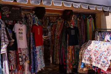 A store with a variety of clothing on display. The clothing is colorful and includes a shirt with the word 