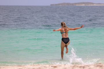 Young woman running into a turquoise colored sea for a swim, Australia.  Summer. Copy space