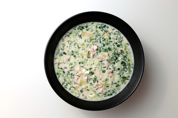 Cold soup with fresh cucumbers, sausage, broth and sour cream in a black plate on a white background. A traditional dish is okroshka.