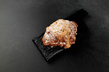Almond croissant. puff pastry, delicate frangipane cream with almonds, enriched with butter. On top, the croissant has a hint of almond flakes and powdered sugar. on a black cutting board