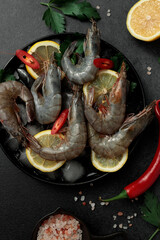 Large King prawns on lemon slices and ice. Hot peppers. Black plate. Black background