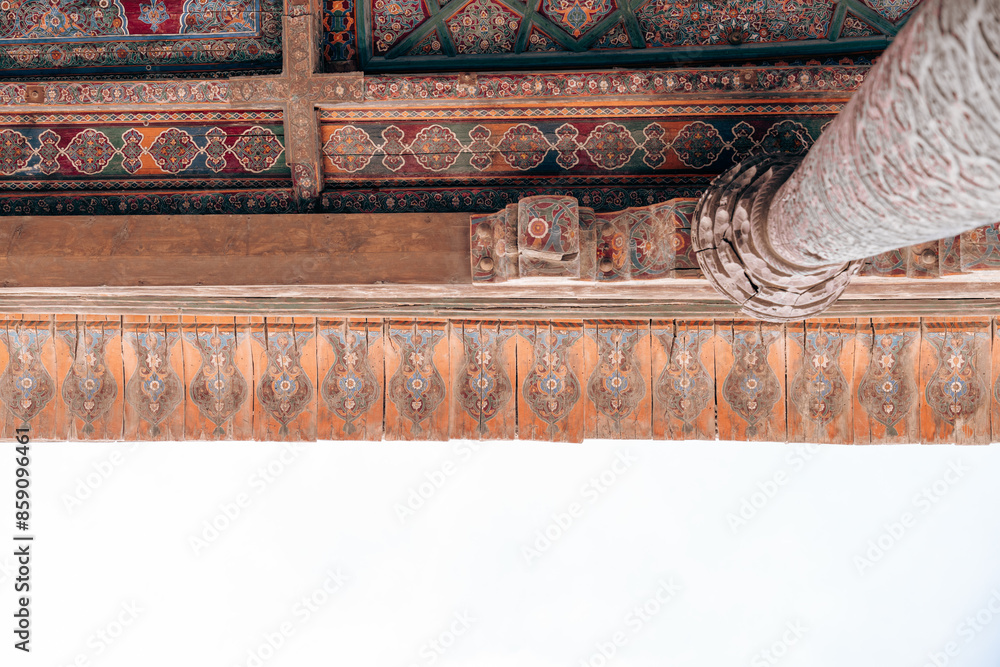 Wall mural A wooden beam with a patterned design on it. The beam is located above a white wall, and the design on the beam is intricate and detailed. Scene is one of elegance and sophistication