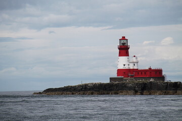 Fototapeta premium A Red and White Coastal Lighthouse on a Rocky Island.