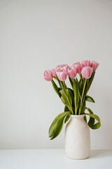 Pink tulip flowers in a clay vase on a table against white background. Soft light, neutral tones. Clean minimalist style with aesthetic vibe
