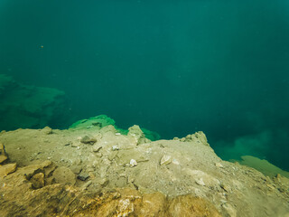 In the middle of the ocean, a rugged shoreline merges electric blue sea with solid rock formations,...