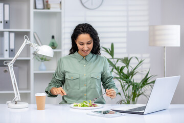 Lunch break at work. Young Latina woman sitting at desk on laptop in office, drinking coffee and...