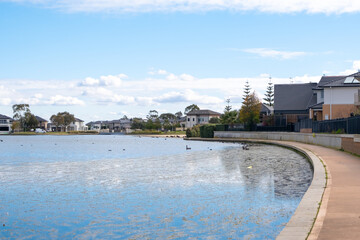 A calm lake surrounded by residential suburban houses and a pedestrian footpath. Beautiful neighborhood in Melbourne's suburbs. Sanctuary Lakes, Point Cook, Australia.