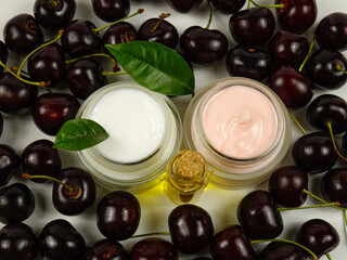 Bottle with cherry seed oil and jars with cherries - based cosmetics, ripe fresh cherries are on a white table
