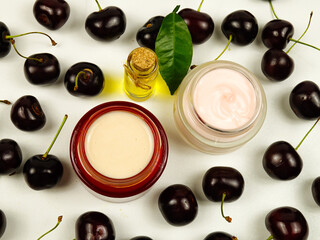 Bottle with cherry seed oil and jars with cherries - based cosmetics, ripe fresh cherries are on a white table
