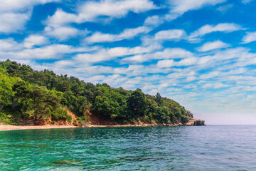 Obraz premium scenic summer landscape of beautiful sea shore with water vawes in bay, green forest on isle rock and nice cloudy sky on background