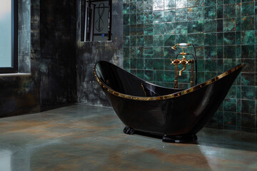 A spacious bathroom featuring a freestanding black bathtub with gold accents, set against a backdrop of dark green tiles. The floor is made of polished concrete.