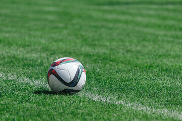 A soccer ball lies on a soccer field with green grass on a white penalty line ready to be kicked by an athlete