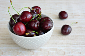 a white bowl of cherries on beige background close up