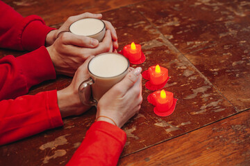 Couple Holding Warm Drinks With Heart Shaped Candles on Wooden Table
