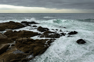 Stormy Ocean Waves Crashing on Rocky Shore with Seaweed and Cloudy Sky.