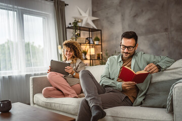 Obraz premium Boyfriend read a book while his girlfriend use tablet at home