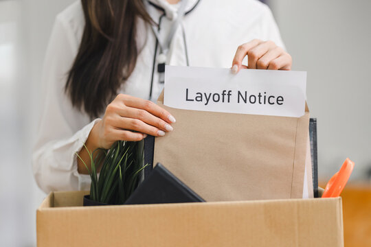 Employee packing personal belongings into cardboard box after receiving layoff notice in modern office.