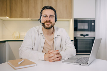Man wearing wireless headset and glasses having online video call meeting in home interior.