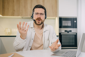 Serious and disappointed businessman with headset for video call, looking at web camera, unhappy talking online meeting