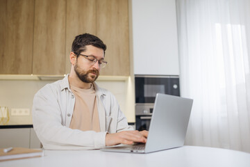 young man freelancer using laptop studying online working from home, happy casual millennial guy typing on pc surfing internet looking at screen enjoying distant job sit at table