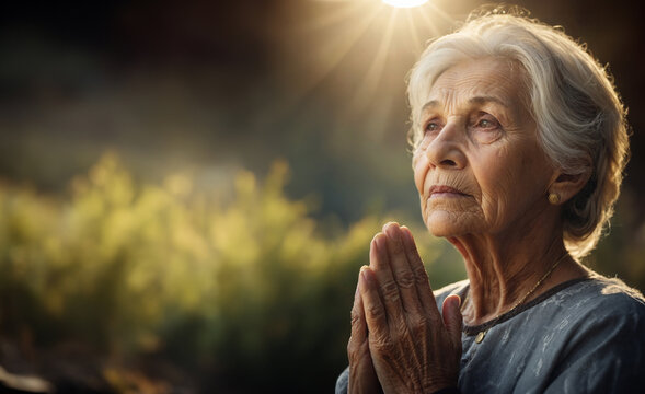 old wise woman with praying hands and with rays of light like Christian Catholic belief concept 