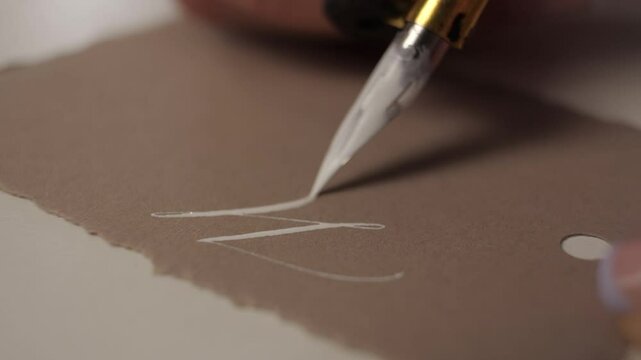 close-up calligraphy. woman applies paint on the nib of the pen for lettering. metallic ink for calligraphy.   brush in hand. beautiful handwriting. penmanship.believe.merry christmas.happy new year
