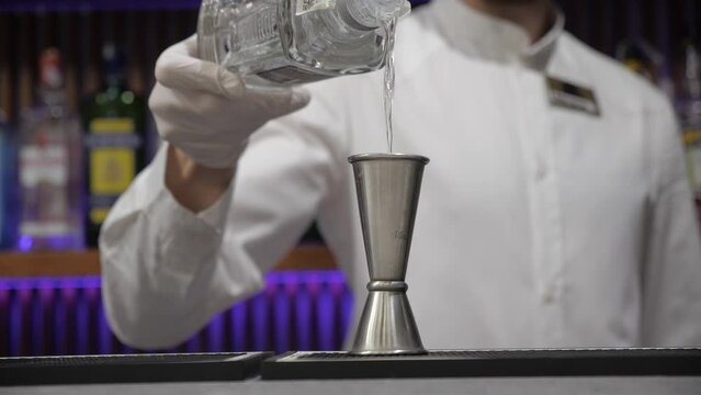 bartender pours vodka in jigger. man in white shirt with gloves. cocktail bar