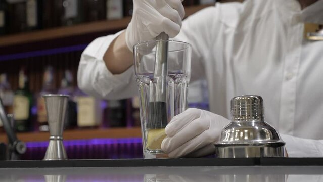 bartender squeezing lemon with muddler. man in white shirt with gloves. cocktail bar