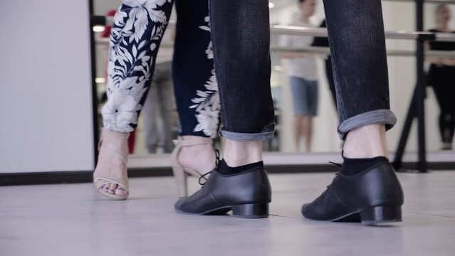 joyful dance practice in the hall on the parquet. reflection of dancing couples in the mirror. teachers show salsa and ballroom dancing movements.female legs in high heel shoes. legs of a man in shoes
