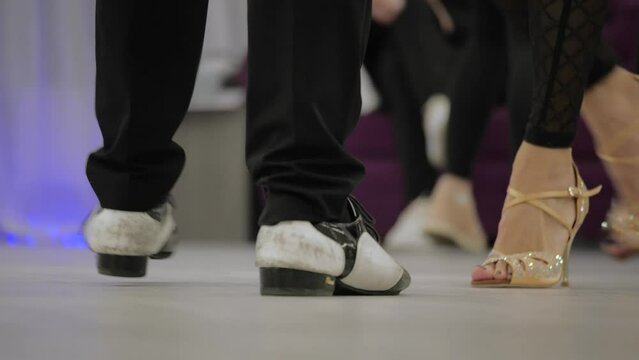 joyful dance practice in the hall on the parquet. reflection of dancing couples in the mirror. teachers show salsa and ballroom dancing movements.female legs in high heel shoes. legs of a man in shoes