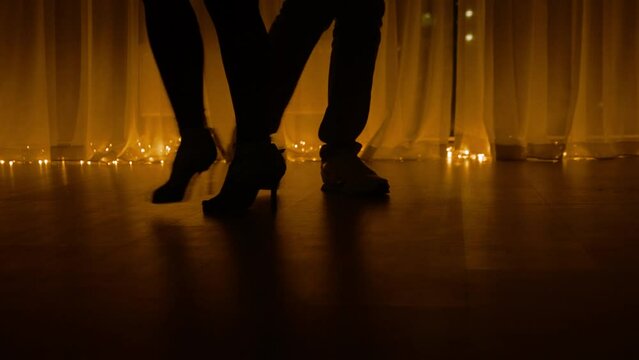 joyful dance practice in dark room. night dance class and party. salsa and ballroom dancing. body silhouette. female legs in high heel shoes. man in shoes. panoramic window with city lights