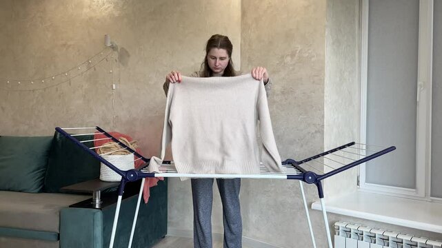 Efficient woman hanging dry laundry on indoor rack in cozy apartment, meticulously organizing clothes in a routine household chore