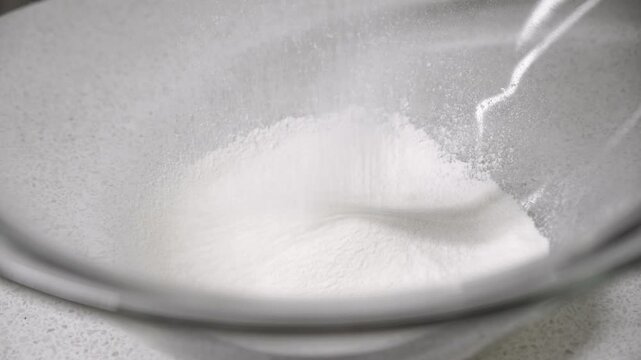 cooking in the kitchen. sifting flour and dry ingredients through a sieve into a glass bowl.
