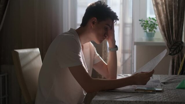 Desperate young guy with documents and bills in the kitchen