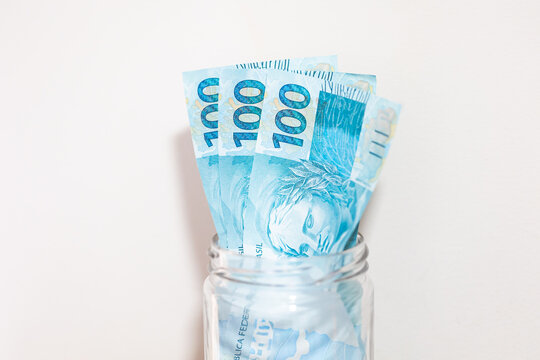 Notas de 100 Reais dentro de um cofrinho de pote de vidro. Dinheiro, Real, Brasil. Finan&ccedil;as, investimentos e economia brasileira. Poupan&ccedil;a, renda fixa ou renda vari&aacute;vel.