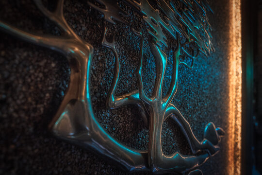 This image shows a close up view of a brass metal bonsai tree sculpture on mid century gravel art wall with dramatic lighting.