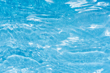Blue water with ripples on the surface. Defocus blurred transparent blue colored clear calm water surface texture with splashes and bubbles. Water waves with shining pattern texture background.
