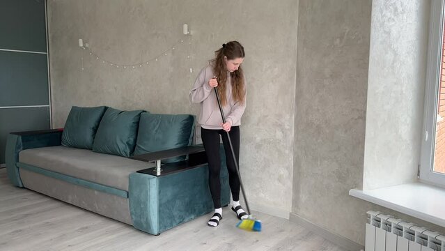Young woman effortlessly maintains a clean and tidy living room in a modern apartment, using a broom to sweep the floor