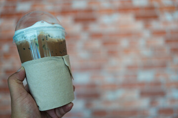 Iced mocha coffee in takeaway cup with brown tissue paper sleeve on hand