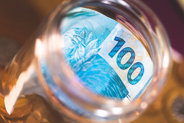 Real, Brasil, Dinheiro. Notas de 100 reais e moedas dentro de um cofrinho de pote de vidro em...