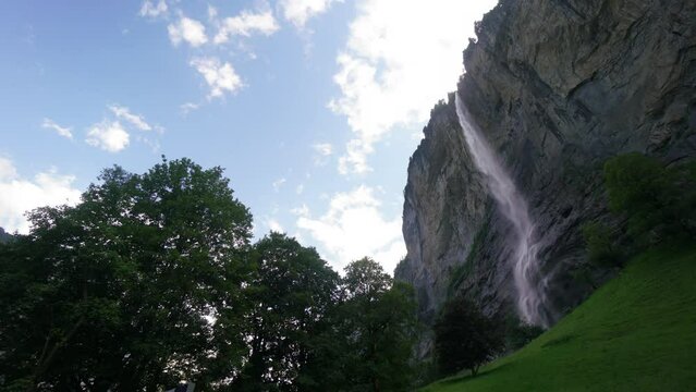 A waterfall cascades down a rocky cliff, surrounded by lush green grass. The scene is serene and peaceful, with the sound of the water creating a calming atmosphere