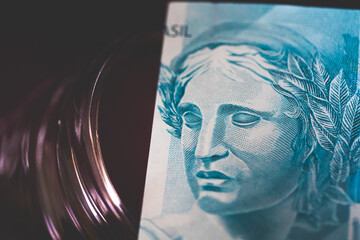 Uma nota de 100 reais em fotografia macro sobre um cofrinho de vidro em fundo escuro ou sombrio....