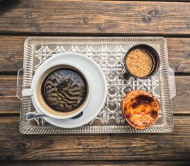 Traditional Portuguese breakfast with black coffee accompanied by a pastel de nata in an indoor patio filled with vegetation in camping site