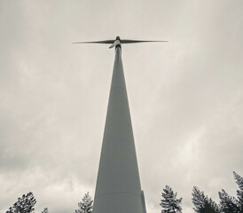 Wide angle shot looking up at windmill rotor with trees populating the bottom of the picture in moody cloudy day