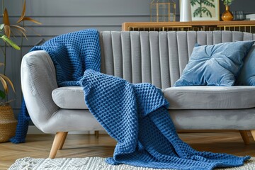 Modern couch with knitted blue blanket in bright interior