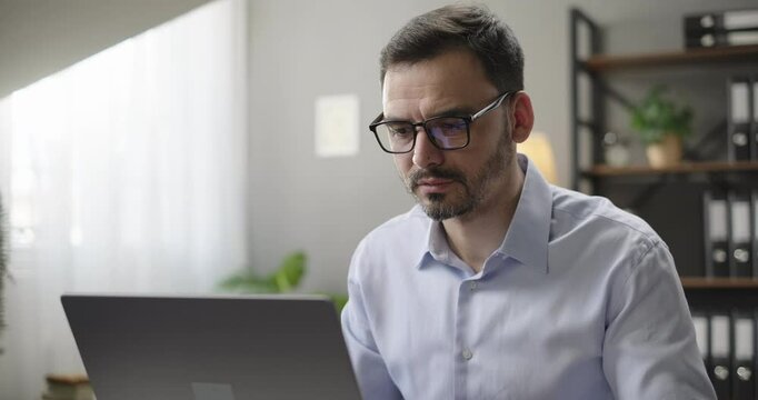 Focused businessman working looking at laptop screen analyzing stock market financial data reading email sitting at the desk