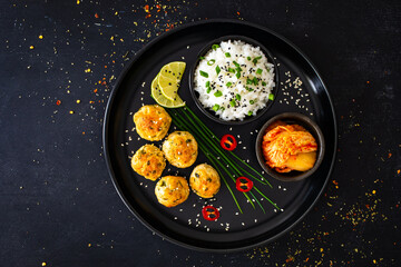 Meatballs served with white rice and kimchi on black plate on black wooden background
