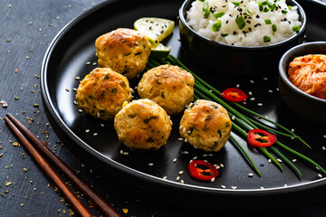 Meatballs served with white rice and kimchi on black plate on black wooden background
