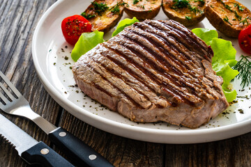 Grilled beef steak with baked potatoes and fresh vegetables on wooden table