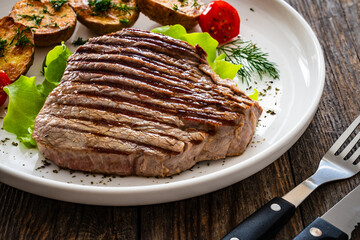 Grilled beef steak with baked potatoes and fresh vegetables on wooden table